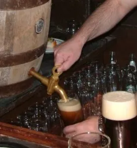 A glass being filled from the tap of a wooden barrel